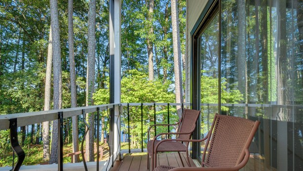 En balkon med fletstole, gelænder i hvidt og udsigt til et skovområde.
