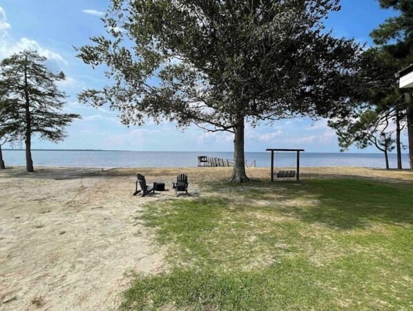 Una zona de playa con un área de césped, dos sillas, una mesita y una estructura de madera.