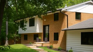 A two-story house with a brick exterior and white siding, featuring a front porch with steps and potted plants. - Tranquil Modern Farmhouse (Waldorf)