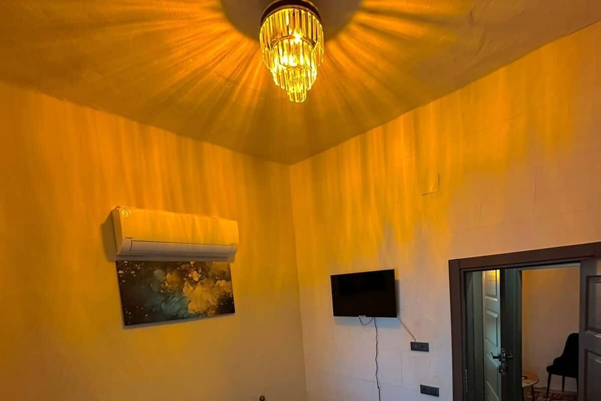 Ein Schlafzimmer mit einem Bett, einem an der Wand befestigten Fernseher, einer Klimaanlage und einer Tür zu einem anderen Raum.