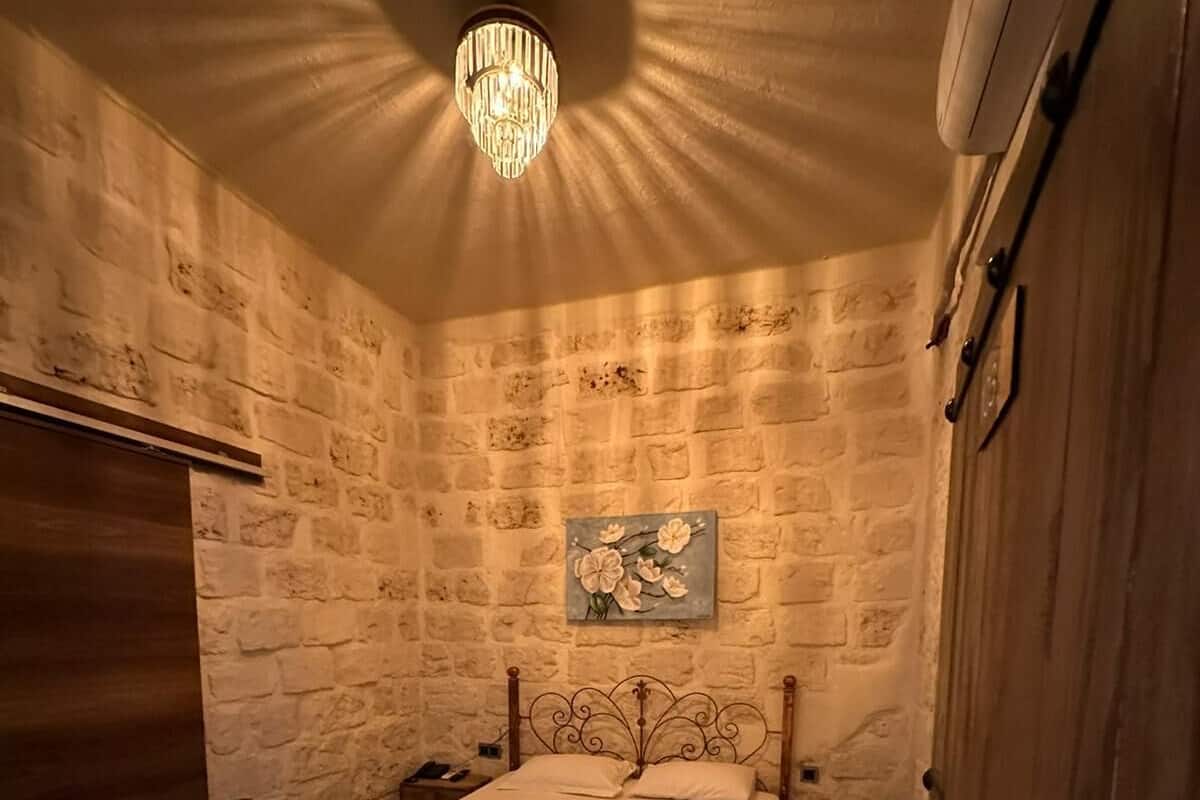 Ein Schlafzimmer mit Steinwand, einem Bett mit dekorativer Kopfteil, einer Chandelüster und einem hölzernen Kleiderschrank.
