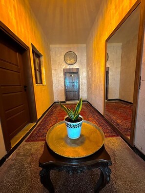 A hallway with a potted plant on a round table, a door, and a wall-mounted clock.