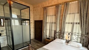 A bedroom with a large bed, a chandelier, a mirror, and a view of the outside. - Sılto's Butik Otel (Mardin)
