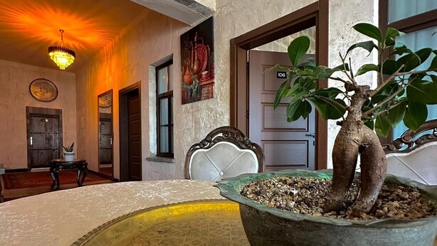 A room with a large, ornate table in the center, a chandelier, and a potted plant with two trunks. - Sılto's Butik Otel (Mardin)