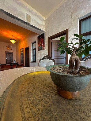 A room with a large, ornate table in the center, a chandelier, and a potted plant with two trunks. - Sılto's Butik Otel (Mardin)