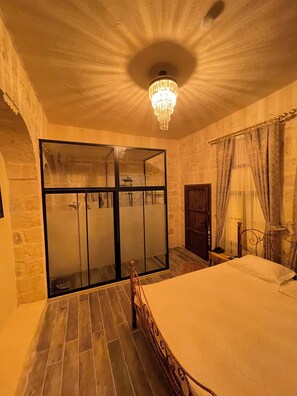 A bedroom with a large bed, a chandelier, a sliding glass door, and stone walls.