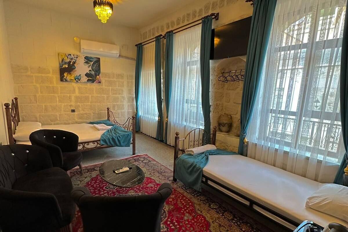 Ein gemütliches Zimmer mit einem Bett, einem Esstisch und Stühlen. Es gibt eine Deckenleuchte, ein Fenster mit Vorhängen und eine wandmontierte Klimaanlage.