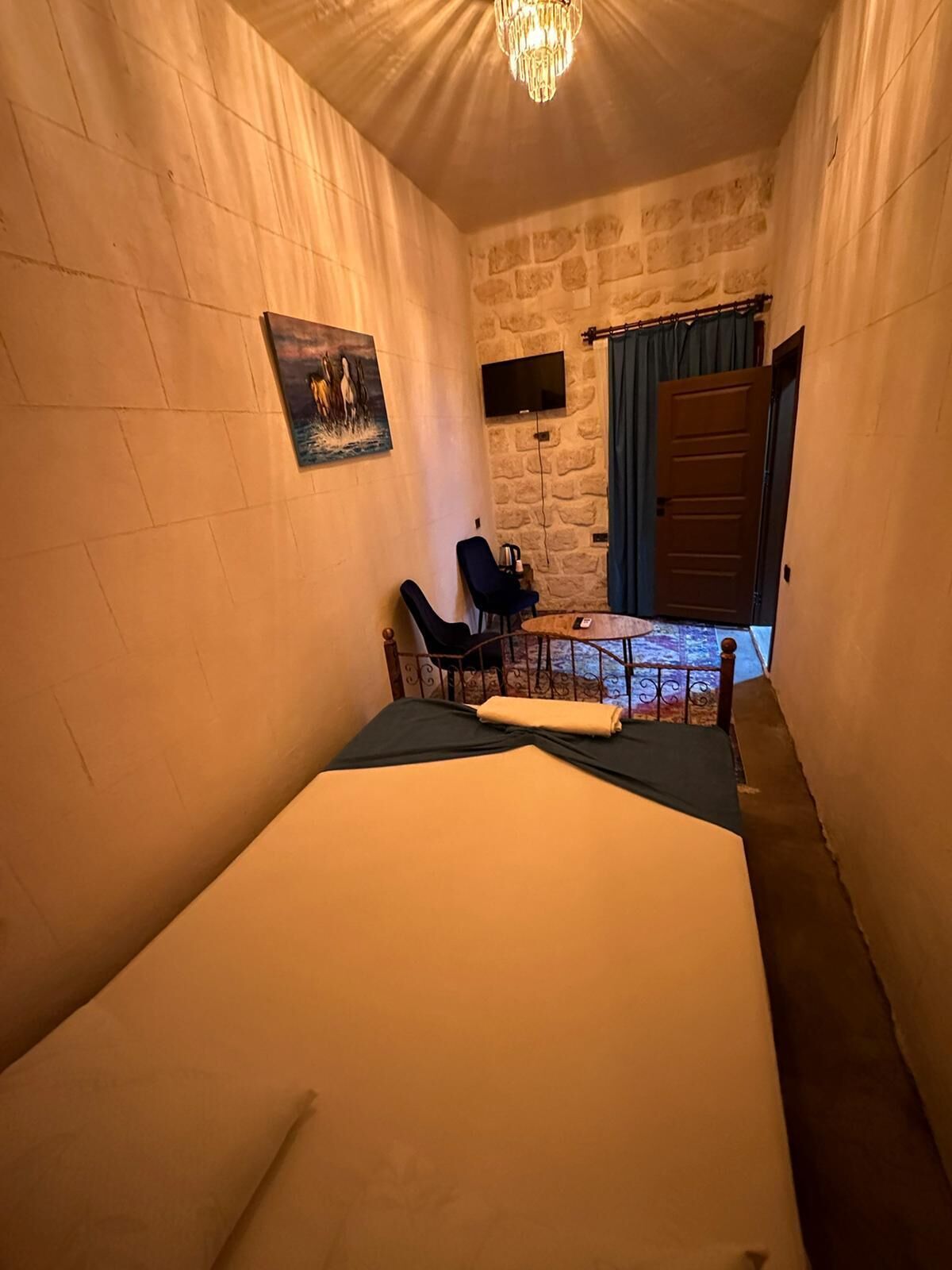 A small, cozy room with a bed, a desk, and a chair. There is a painting on the wall and a window with curtains.