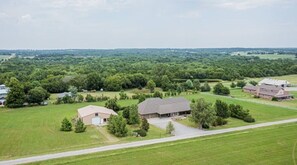 An aerial view of a rural property with multiple buildings, including a large barn and smaller structures, surrounded by lush green fields and trees.