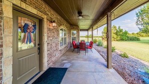A covered porch with a brick exterior, a door with a bow decoration, and a table with chairs.