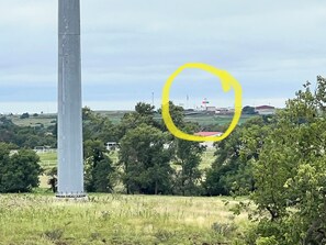 Standing tall in a serene landscape, a utility pole rises amidst a grassy field with a red-roofed building in the distance.