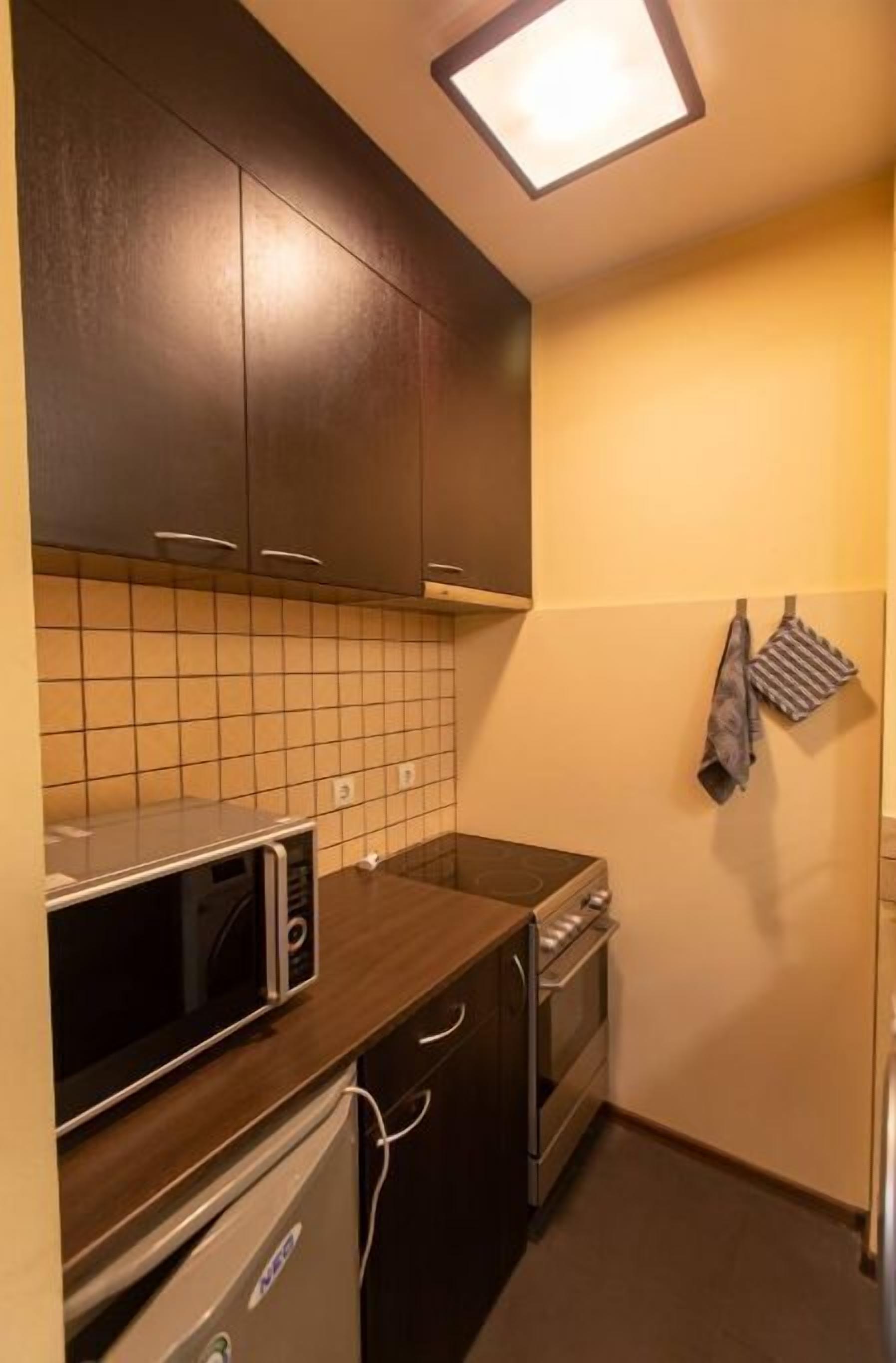 A compact kitchen with dark cabinets, a microwave, an oven, and a tiled backsplash.