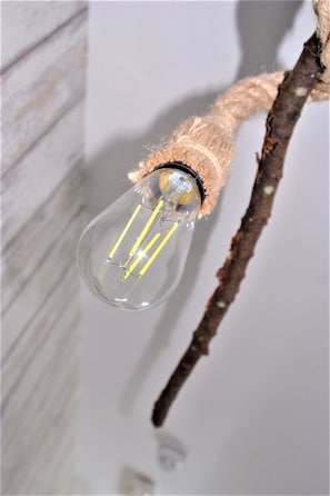 A clear glass light bulb with yellow filament wires, attached to a branch with a rope. - The Anchor (Ely)