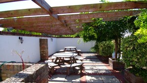 Un patio al aire libre con mesas y bancos de madera, un muro de ladrillo y una pérgola.