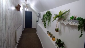 Un pasillo con pared de madera, un radiador, una puerta y una pared blanca con plantas colgantes y una estantería.