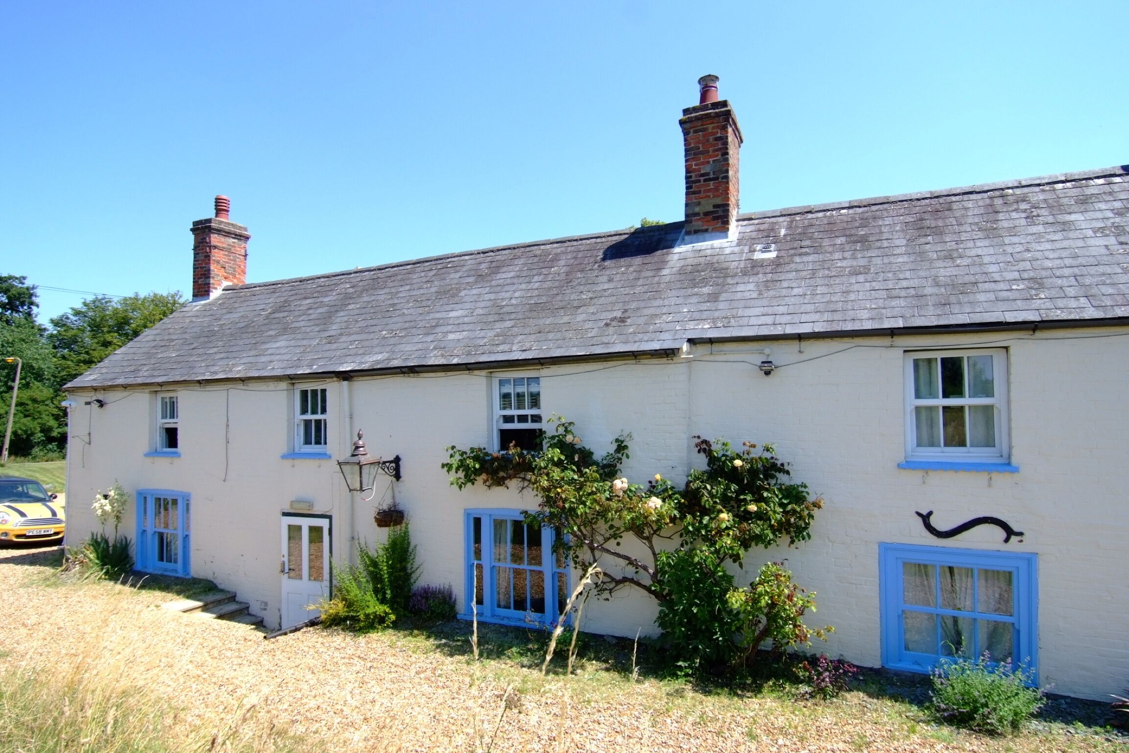 A two-story house with a white exterior and blue accents, featuring a chimney, multiple windows, and a small garden area.