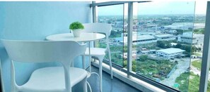 A balcony with white chairs and a small table, overlooking a cityscape with buildings and greenery. - The White Bali Staycation Unit at Azure North
 (San Fernando)