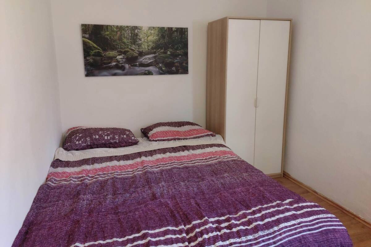 A bedroom with a bed, a wardrobe, and a painting of a forest scene.