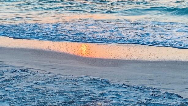 Une plage avec des vagues et un coucher de soleil.