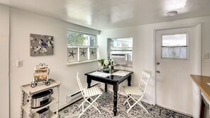 Un coin repas comprenant une table noire, des chaises blanches, un élément décoratif mural, une fenêtre et une porte.