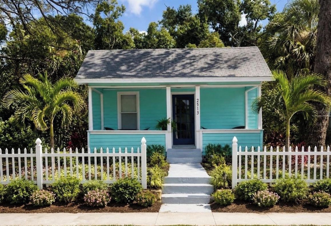 A small, single-story house with a white picket fence, a front porch, and a mailbox.