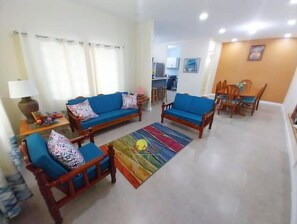 Un salon comprenant un canapé, deux fauteuils, une table basse et un coin repas avec une table et des chaises.