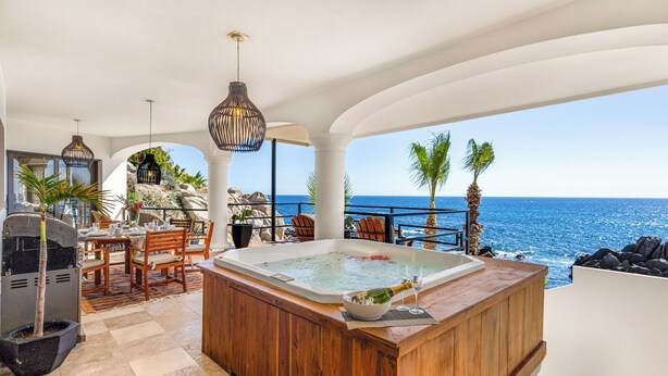 A luxurious outdoor seating area with a hot tub, wooden furniture, and a view of the ocean.