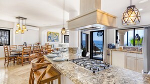 A modern kitchen with granite countertops, wooden chairs, and pendant lighting.