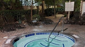 A hot tub with a tiled edge, surrounded by lounge chairs and a brick patio.