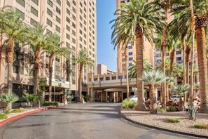 A hotel entrance with a modern design, palm trees, and a clear sky. - Las Vegas | Pool & Strip Access | City Lights Stay (Las Vegas)