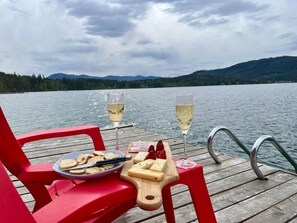 Un muelle de madera con una silla roja, un plato de comida y dos copas de champán.