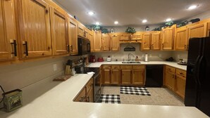 A kitchen with wooden cabinets, a black refrigerator, and a checkered mat on the floor. - Cabin close to Helen and Water (Hiawassee)
