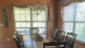 A dining room with a wooden table and chairs, large windows with blinds, and a chandelier. - Cabin close to Helen and Water (Hiawassee)