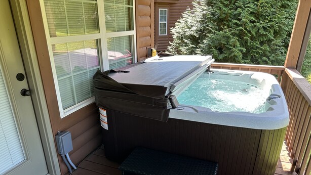 A hot tub on a wooden deck with a small bench, a window, and a door. - Cabin close to Helen and Water (Hiawassee)