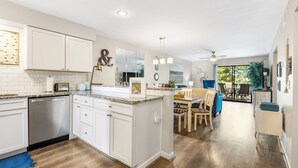 A modern kitchen with white cabinetry, a dishwasher, and a dining area with a table and chairs. - Pointe Royale*Autumn Stay*KING Beds* (Branson)