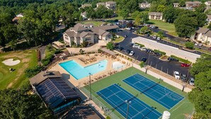 An aerial view of a residential area with a swimming pool, tennis courts, and a solar panel array. - Pointe Royale*Autumn Stay*KING Beds* (Branson)