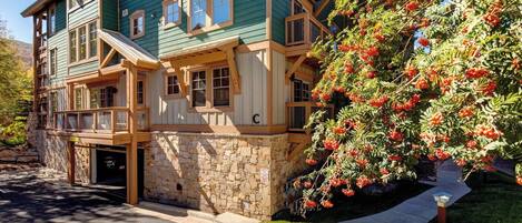 A multi-story building with a stone foundation, wooden balconies, and a large tree with red berries.