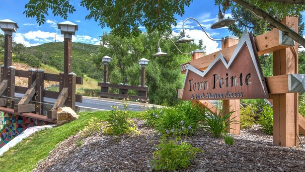 A wooden sign with 'Tow Pointe & Park Station Access' written on it, surrounded by a landscaped area with mulch and small plants. - Town Pointe by KBM (Park City)