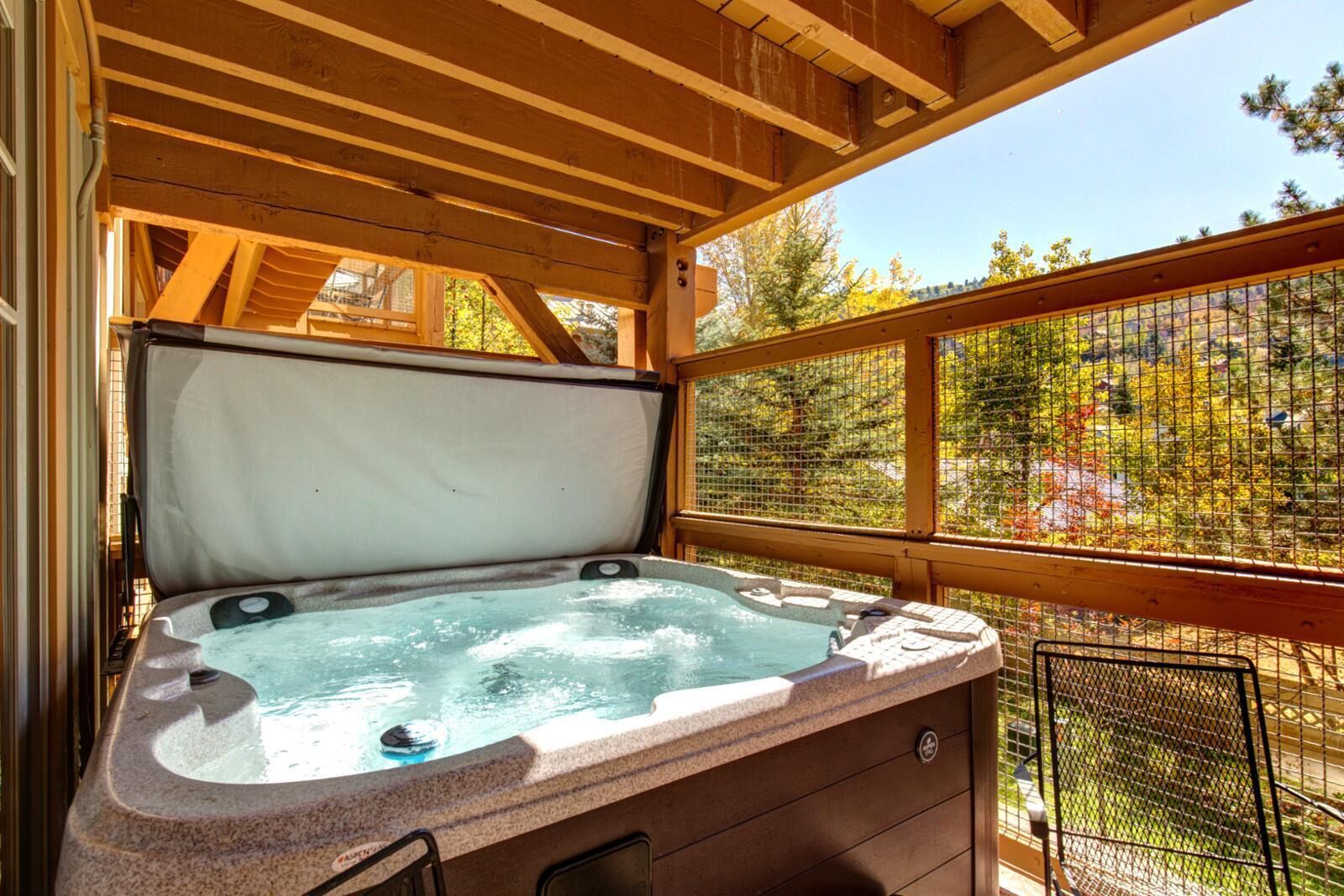 Un bain à remous doté d’une terrasse en bois et entouré d’une clôture en treillis, le tout niché au milieu des arbres.