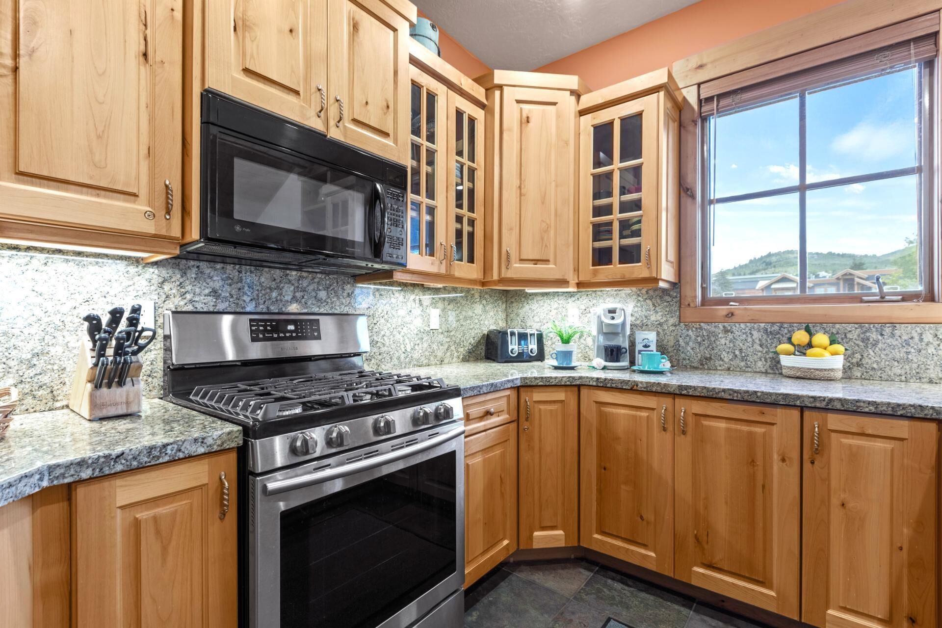 A kitchen with wooden cabinets, a stainless steel stove, a microwave, and a window with a view.