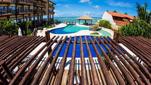 A resort with a pool, wooden deck, and a view of the ocean. - Cond. Barra Bali | Frente ao Mar | Destino BSM 108 (Barra de São Miguel)