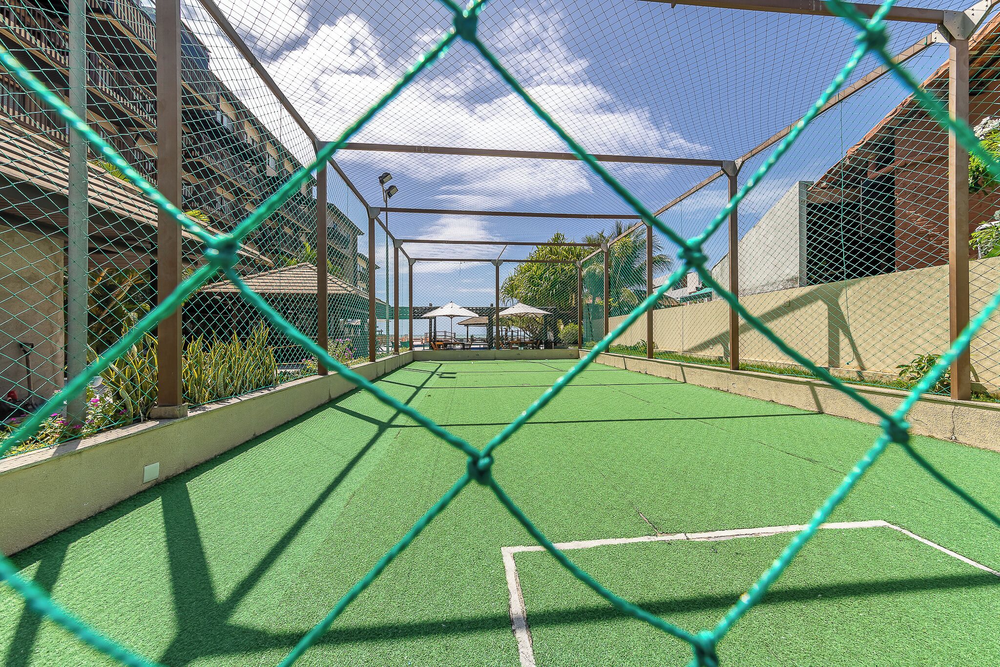 Cancha deportiva vallada con superficie verde, rodeada de edificios y un cielo despejado.