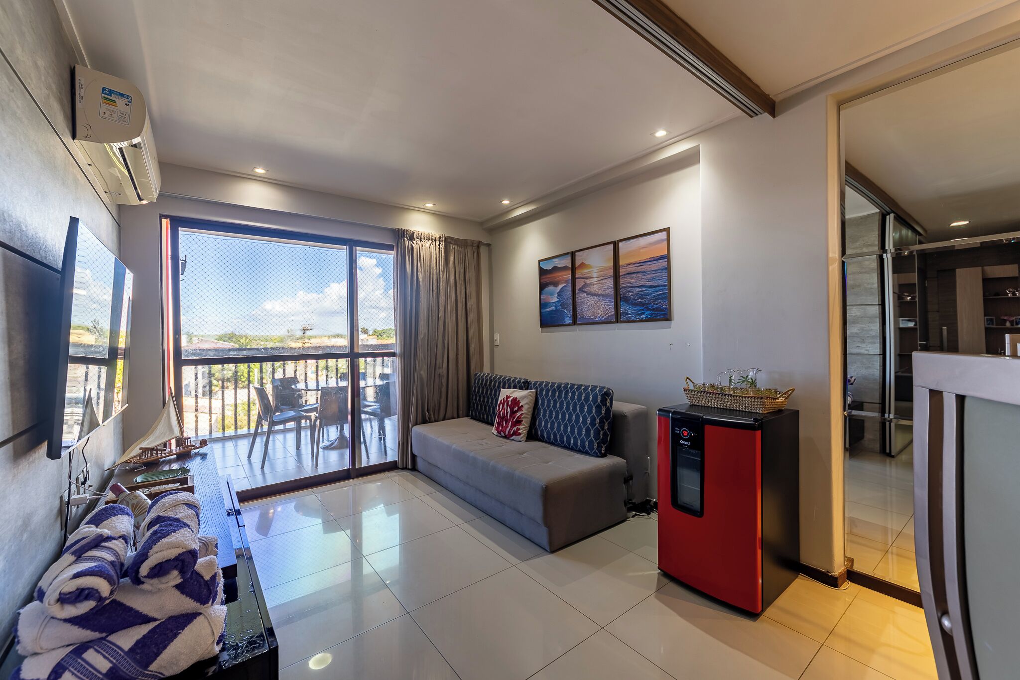 A modern living room with a sofa, a small refrigerator, and a balcony with a view.