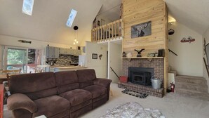 Ein gemütliches Wohnzimmer mit einem braunen Sofa, einem Kamin und einer Küche im Hintergrund.
