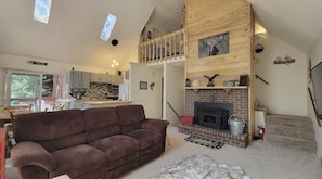 A cozy living room with a brown sofa, a fireplace, and a kitchen in the background.