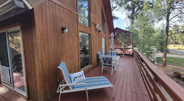 A wooden deck with outdoor seating, including a lounge chair and a table with chairs.