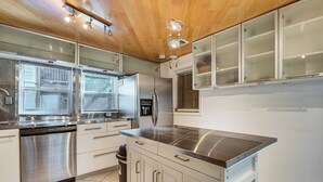 Una cocina moderna con electrodomésticos de acero inoxidable, armarios blancos y techo de madera.