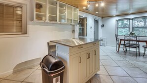 Una cocina con encimera de acero inoxidable, un cubo de basura y una zona de comedor con mesa y sillas.