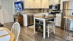 A modern kitchen with white cabinets, stainless steel appliances, and a wooden dining table. - Tranqulity and relaxtion destination (Syracuse)