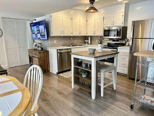 A modern kitchen with white cabinets, stainless steel appliances, and a wooden dining table. - Tranqulity and relaxtion destination (Syracuse)